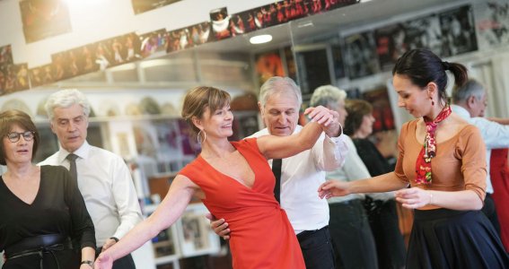 Eine junge Frau überprüft die Tanzschritte eines Seniorenpaares