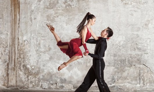 Eine weibliche Tänzerin posiert in einer Tanzbewegung in der Luft und stützt sich auf ihren Tanzpartner