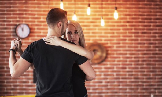 Eine junge Frau und ein junger Mann tanzen eine Paartanz vor einer Ziegelwand