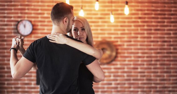 Eine junge Frau und ein junger Mann tanzen eine Paartanz vor einer Ziegelwand