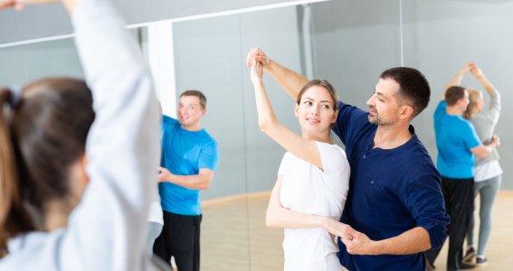 Mehrere junge Menschen tanzen einen Paartanz in einem Raum mit Spiegelwänden