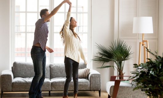 Ein junges Paar tanzt lachend im Wohnzimmer