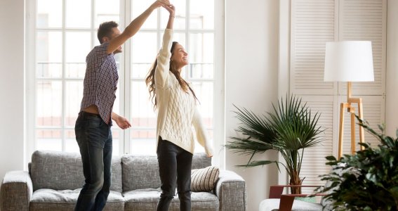 Ein junges Paar tanzt lachend im Wohnzimmer