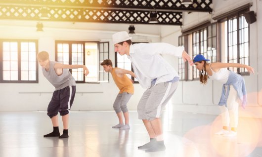 Vier Jugendliche tanzen in legerer Kleidung in einem leeren Raum