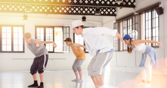 Vier Jugendliche tanzen in legerer Kleidung in einem leeren Raum