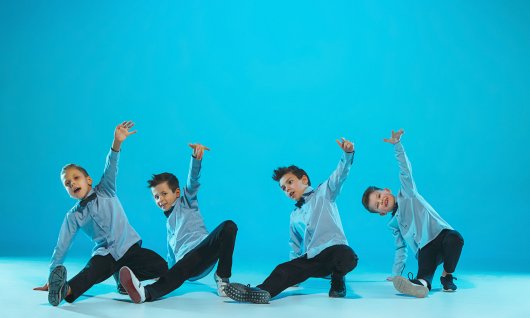 Vier jungen in blauen Hemden posieren in Breakdance-Pose vor blauem Hintergrund