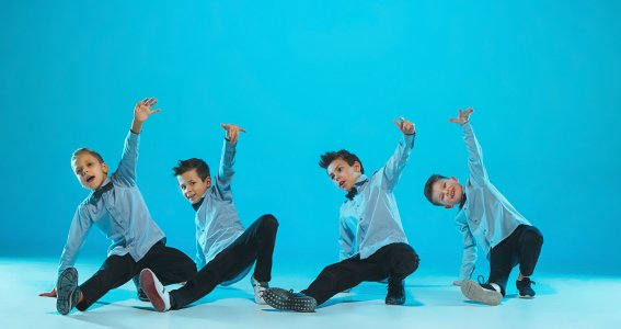 Vier jungen in blauen Hemden posieren in Breakdance-Pose vor blauem Hintergrund
