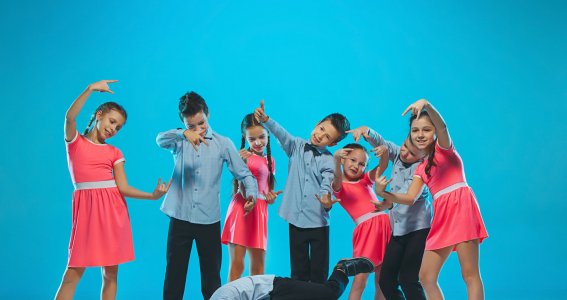 Eine Gruppe von Jungen und Mädchen in blauen und rosafarbenen Kostümen tanzen im Kreis und posieren