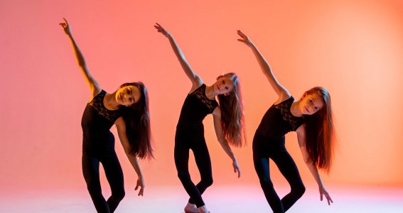 Drei Mädchen mit langen offenen Haaren beugen sich im Tanzschritt auf die Seite
