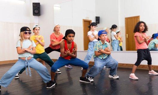 Eine Gruppe von Kindern in sportlicher Kleidung tanzen synchron Hip Hop in einem Raum mit Spiegelwand