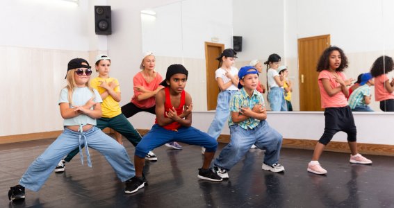 Eine Gruppe von Kindern in sportlicher Kleidung tanzen synchron Hip Hop in einem Raum mit Spiegelwand