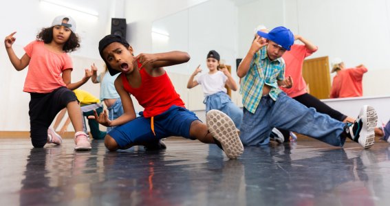 Mehrer Kinder in cooler Kleidung posieren auf dem Boden des Tanzstudios