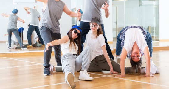 Eine junge Tanzgruppe aus Mädchen und Jungs posieren vor einer Spiegelwand in einer Hip Hop Formation