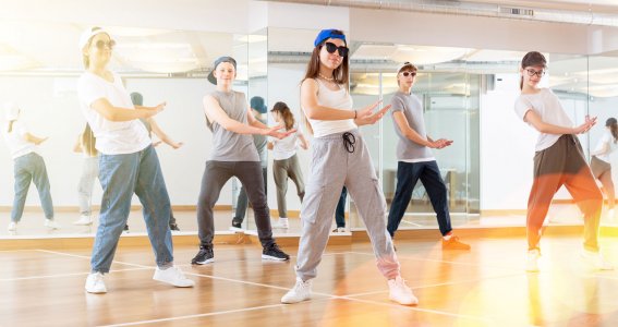 Mehrere Jugendliche tanzen in einem Tanzstudio mit coolen Kappen und Sonnenbrillen und posieren