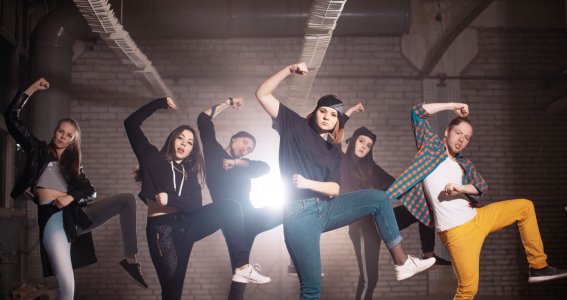 Eine Gruppe Jugendlicher tanzt Hip Hop in lässiger Kleidung in einem Industrieraum