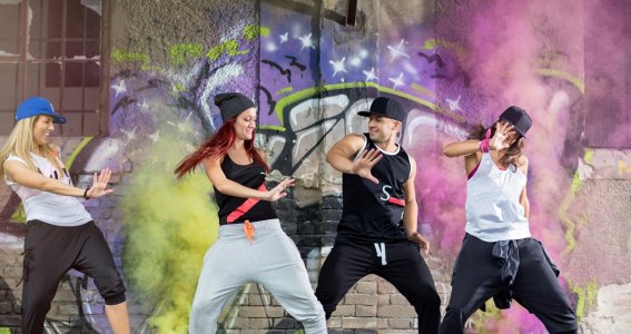 Vier junge Menschen tanzen vor einer Graffiti Wand Hip Hop 