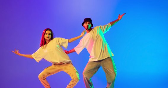 Ein junger Mann und eine junge Frau tanzen mit Kniebewegungen vor einem blauen Hintergrund