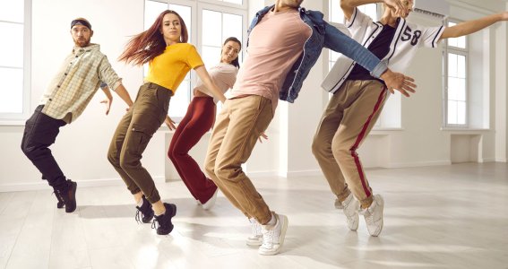 Junge Männer und Frauen tanzen in einem leeren Raum und stehen nach hinten geneigt auf den Zehenspitzen