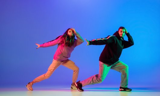 Ein junger Mann und eine junge Frau tanzen in legerer Kleidung vor blauem Hintergrund