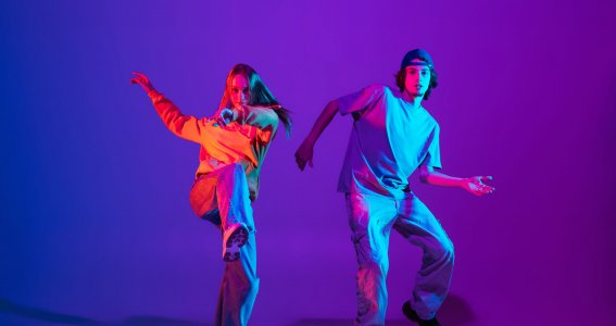 Zwei Jugendliche tanzen in lockerer Kleidung vor violettem Hintergrund