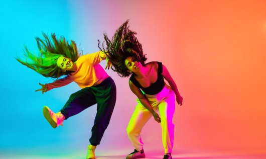 Zwei tanzende Frauen in sportlicher Kleidung beugen sich vor und schwingen ihre Haare 