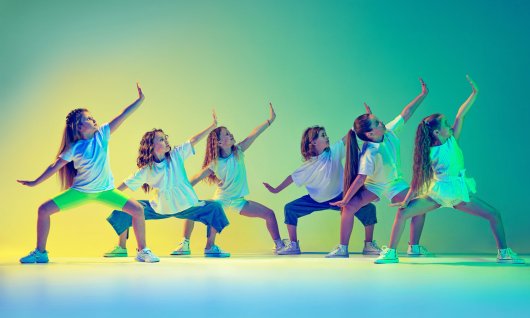 Eine Gruppe junger Mädchen in weißen T-shirts und Shorts tanzen in einer Formation mit seitlich ausgestreckten Armen und seitlichem Blick