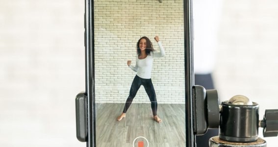 Eine Frau filmt sich auf dem Handy wie sie vor einer Ziegelwand tanzt