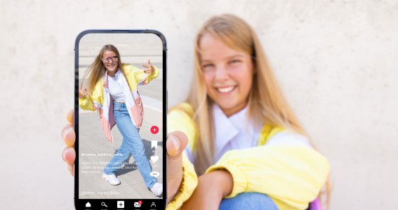 Ein Mädchen sitzt auf dem Boden und präsentiert ein Video von sich tanzend auf dem Handy