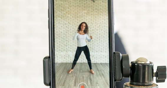 Eine Frau tanzt vor einer Ziegelwand und filmt sich dabei auf ihrem Handy
