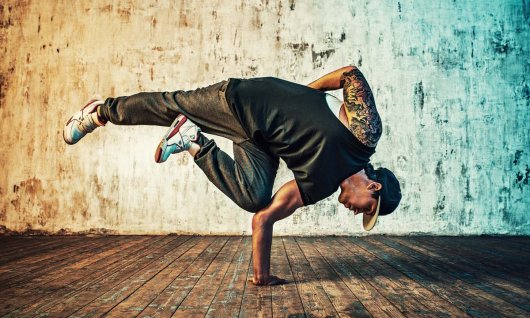 Ein Mann in dunkler Kleidung posiert in Breakdance Position
