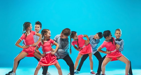 Eine Tanzgruppe von Mädchen und Jungs in pinken und blauen Kostümen vor blauem Hintergrund