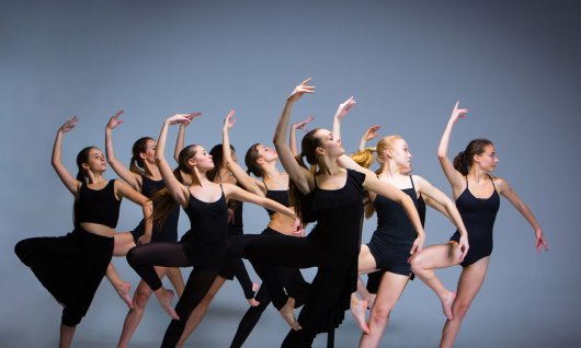 Eine Tanzgruppe in schwarzen Turnoutfits mit einer Tanzbewegung im Ballettstil