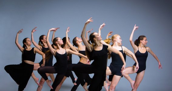 Eine Tanzgruppe in schwarzen Turnoutfits mit einer Tanzbewegung im Ballettstil