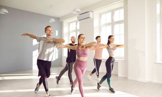 Fünf junge, lachende Menschen tanzen in einem hellen, leeren Raum