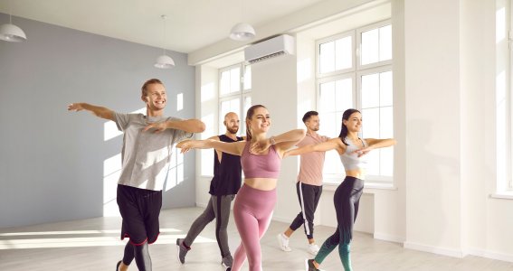 Fünf junge, lachende Menschen tanzen in einem hellen, leeren Raum