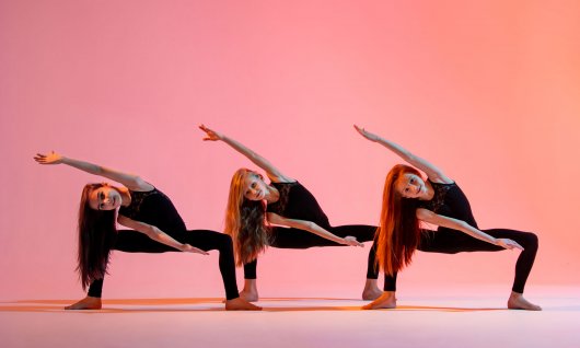 Drei Mädchen mit langen Haaren tanzen in schwarzer Kleidung vor pinkem Hintergrund