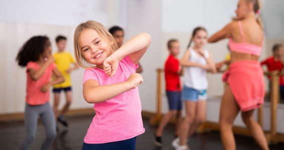 Ein Mädchen posiert im Tanzstudio, mit der Tanzgruppe im Hintergrund