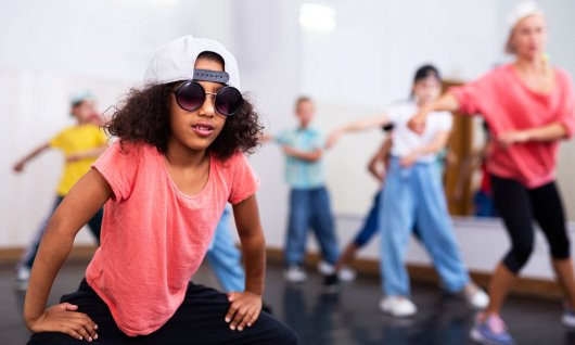 Ein junges Kind posiert in Kappe und Sonnenbrille mit der Tanzgruppe im Hintergrund