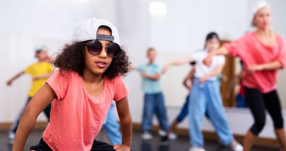 Ein junges Kind posiert in Kappe und Sonnenbrille mit der Tanzgruppe im Hintergrund