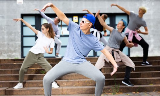 Jugendliche tanzen posierend vor einem Gebäude auf den Stufen
