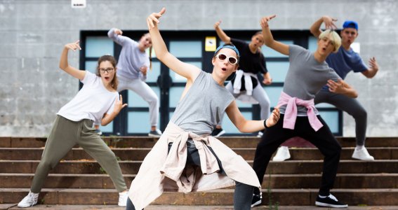 Eine Gruppe Jugendlicher tanzt vor einem Gebäude auf den Stufen und posiert
