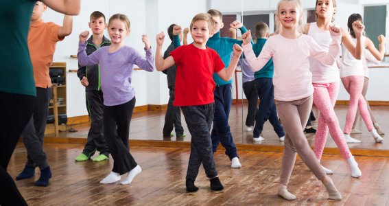Kinder überkreuzen in einem Tanzstudio die Füße und halten die Hände hoch