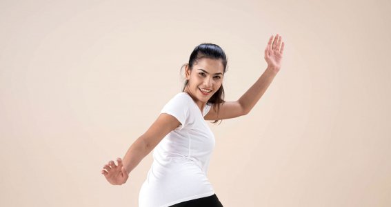 Eine junge Frau in weißem T-Shirt und schwarzer Hose posiert in einer Tanzbewegung