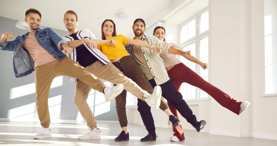 Eine Gruppe lachender, junger Menschen steht in einer Reihe und streckt ein Bein seitlich nach vorne