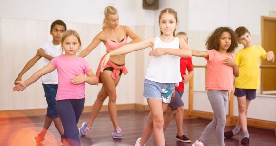 Eine Gruppe von Kindern tanzt in einem Tanzstudio und streckt die Arme seitlich weg