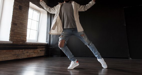 Ein junger Mann in zerrissener Jeans tanzt in einem leeren Raum mit Ziegelwand