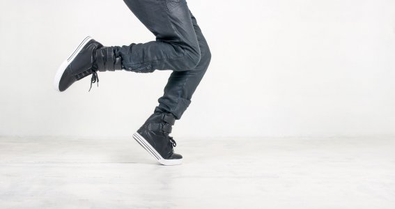 Tanzende Männerfüße in dunkler Hose und schwarzen, sportlichen Schuhen