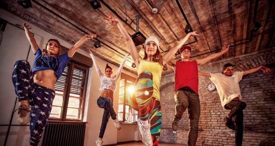 Jugendliche tanzen in einem Tanzstudio mit Ziegelwänden und strecken Knie und Arme nach oben