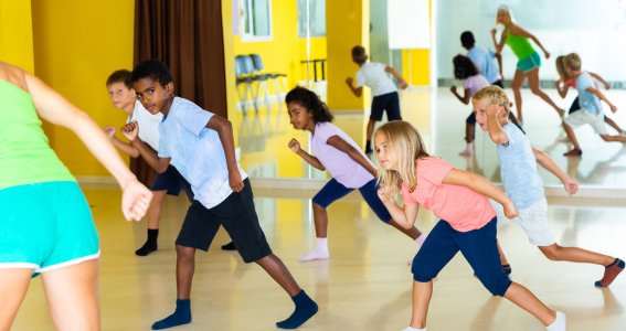 Kinder tanzen in bunter Kleidung vor einer Spiegelwand