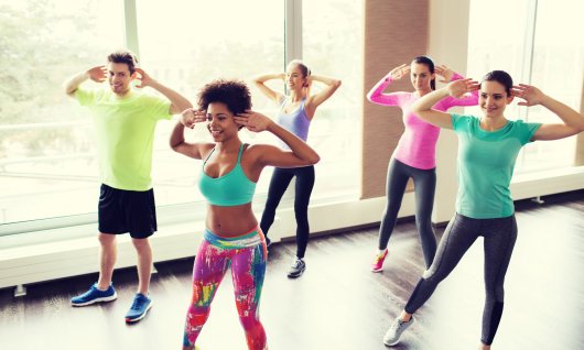 Eine Gruppe junger Menschen tanzt in sportlicher Kleidung vor einer Fensterwand